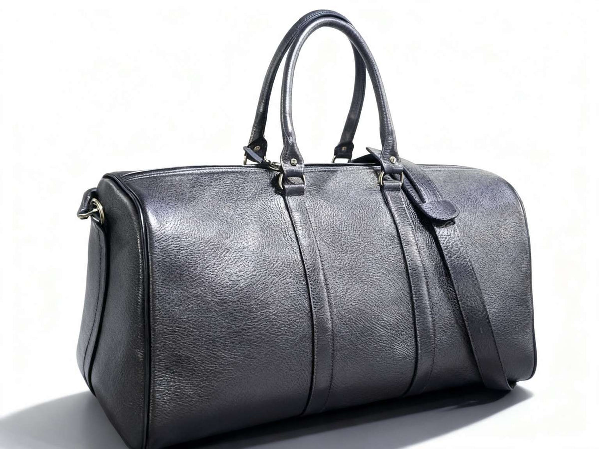 Black leather duffel travel bag with twin handles and shoulder strap on white background