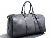 Black leather duffel travel bag with twin handles and shoulder strap on white background