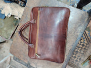 Brown leather briefcase on artisan workbench, exterior zipped compartment and stitched corners