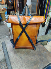 Cognac leather roll-top backpack photographed in Moroccan workshop, black cross straps and brass-tone buckles