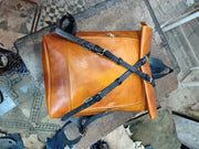 Cognac roll-top leather backpack from above, showing crossover black fastening straps and buckles