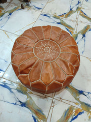 Tan round leather pouf with cream Moroccan geometric flower embroidery viewed from above